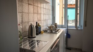 A kitchen with a white countertop, a stove, a kettle, and a window with a view of a balcony. - Panoramic apartment with large roof terrace in Naples, view of harbor, Vesuvius (Neapel)