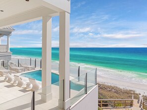 Un balcon doté d’une balustrade en verre, donnant sur une plage et une piscine.