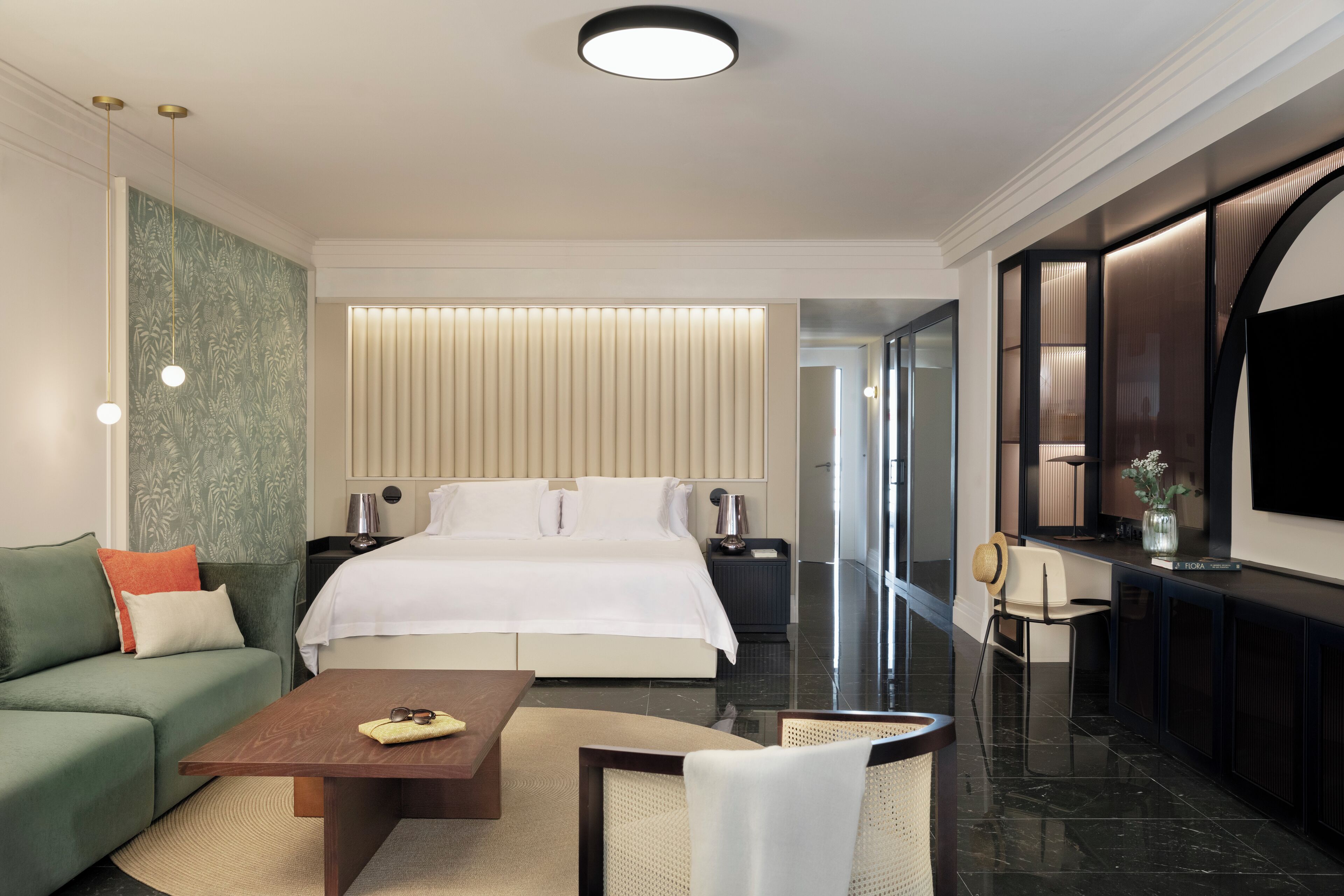 A modern hotel room with a large bed, a sofa, a coffee table, and a TV.
