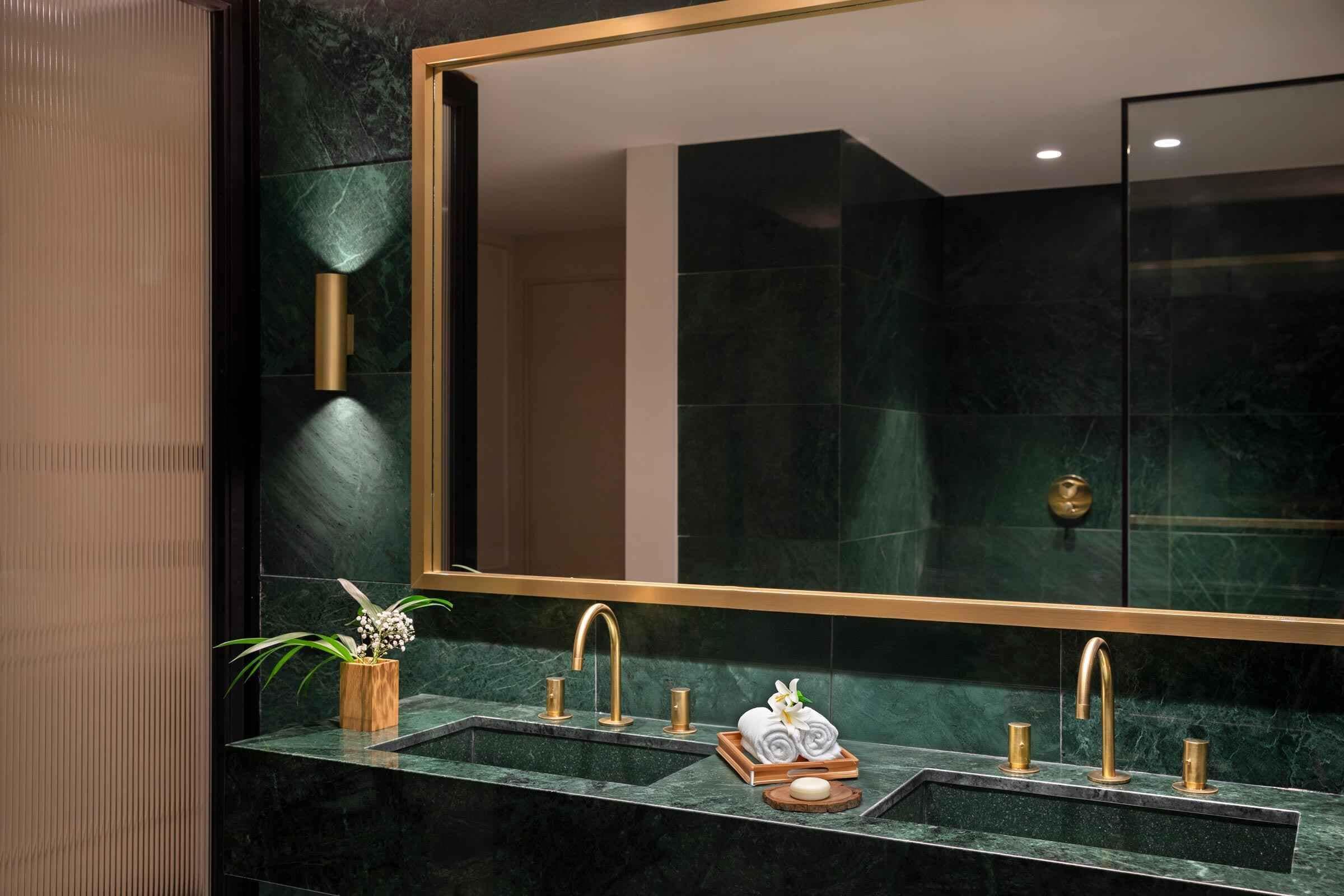 Un baño moderno con un espejo grande, dos lavamanos con grifos dorados y una planta en maceta.