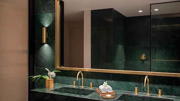 Un baño moderno con un espejo grande, dos lavamanos con grifos dorados y una planta en maceta.