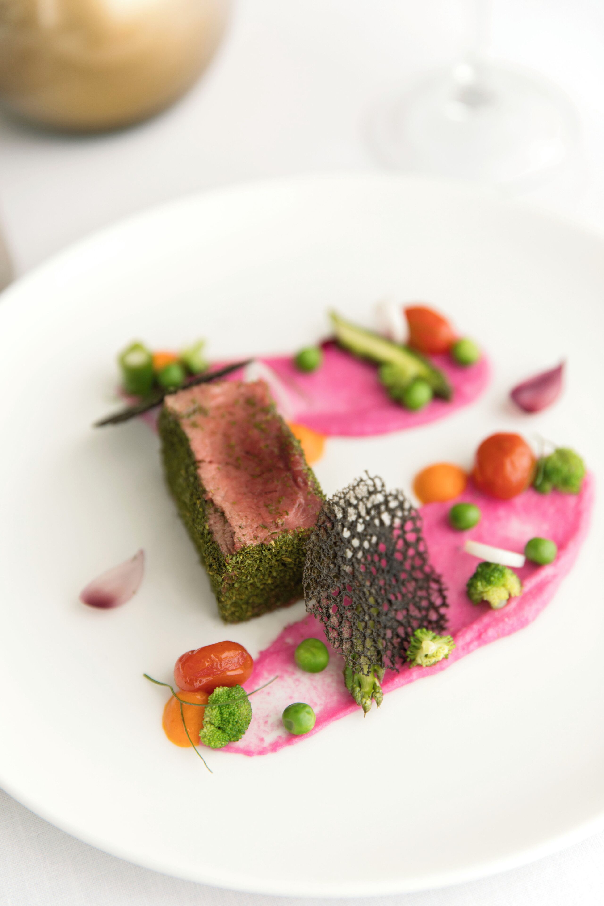 Un plato blanco con carne, verduras verdes y salsa rosa.
