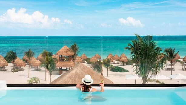 A woman relaxing in a pool with a view of a beach and ocean. - Excellence Coral Playa Mujeres - Adults Only All Inclusive (Punta Sam)