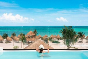 A woman relaxing in a pool with a view of a beach and ocean. - Excellence Coral Playa Mujeres - Adults Only All Inclusive (Punta Sam)