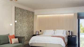 A modern hotel room with a large bed, a sofa, a nightstand with a lamp, and a view of the outdoors.