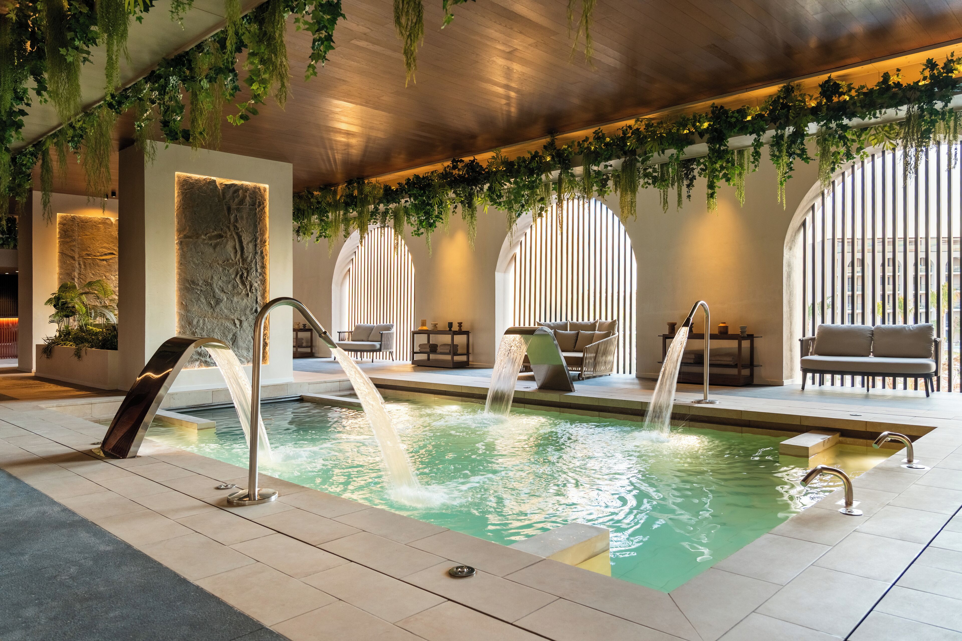 An indoor pool with multiple water features, seating areas, and greenery.