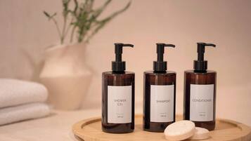 Trois flacons de gel douche, de shampoing et d’après-shampoing, présentés sur un plateau en bois avec deux savons.