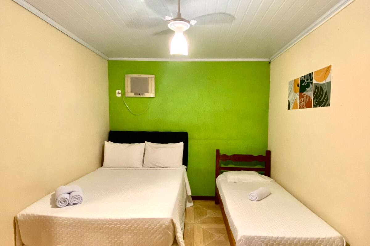 Ein Zimmer mit zwei Betten, einem Deckenventilator, einer Wand-Klimaanlage und einer grünen Akzentwand.
