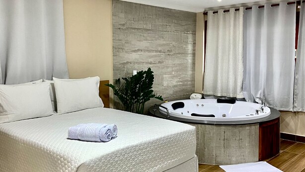 Une chambre à coucher moderne avec un grand lit, une salle de bain séparée dotée d’un jacuzzi et une palette de couleurs neutres.