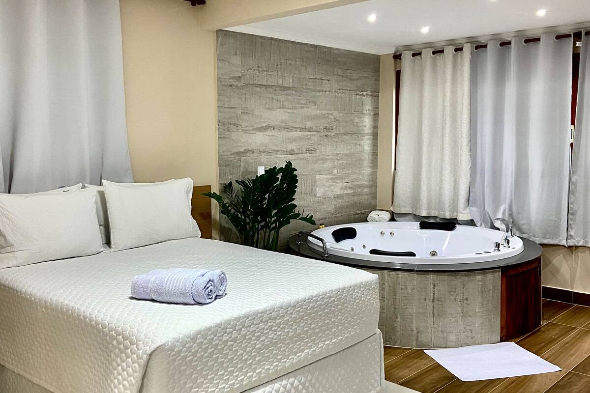 Ein modernes Schlafzimmer mit einem großen Bett, einem separaten Badezimmer mit Whirlwanne und einer neutralen Farbgestaltung.