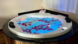 Un bain à remous où flottent des pétales de rose, entouré d’un sol en bois et d’un cadre noir.