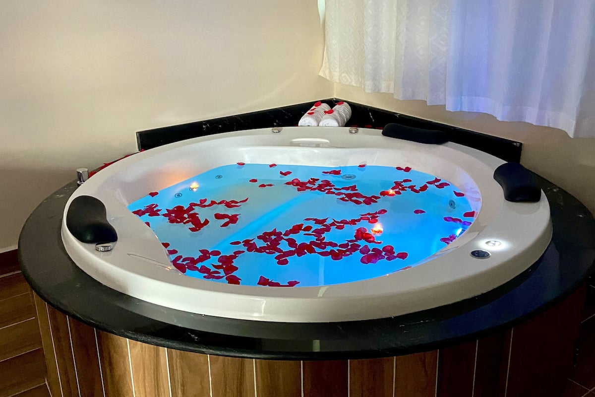Ein Whirlpool mit darin treibenden Rosenblättern, umgeben von Holzboden und einem schwarzen Rahmen.
