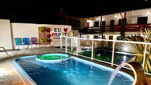Une piscine agrémentée d’un élément décoratif aquatique, entourée de chaises longues et bordée d’un mur sur lequel est apposée une enseigne.