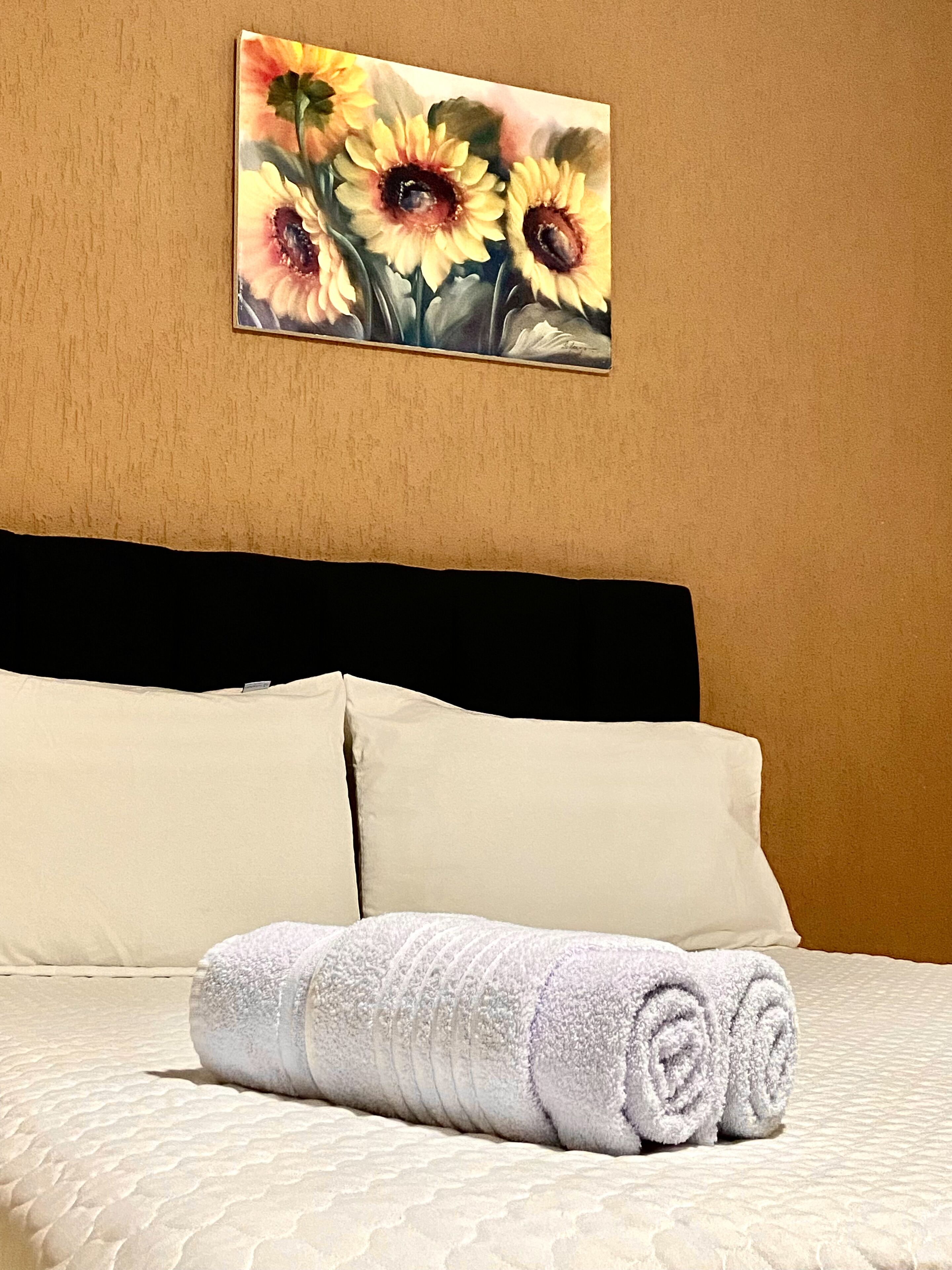 Cama bem arrumada com duas almofadas e uma toalha branca enrolada.