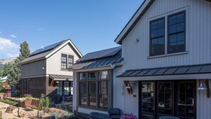Une maison moderne à deux étages, dotée de grandes fenêtres, d’un patio couvert et d’un jardin bien entretenu.