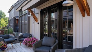 Un espace extérieur abrité, aménagé avec des meubles en osier, de grandes fenêtres et un luminaire suspendu.