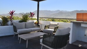 A covered outdoor seating area with a sofa and chairs, a table, and potted plants. - Amazing views coastal apartment. 2BD (Puerto Vallarta)