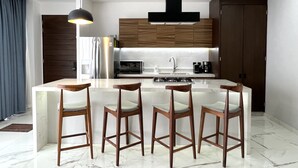 A modern kitchen with a central island, four bar stools, a stainless steel refrigerator, a microwave, a gas stove, and wooden cabinets. - Amazing views coastal apartment. 2BD (Puerto Vallarta)