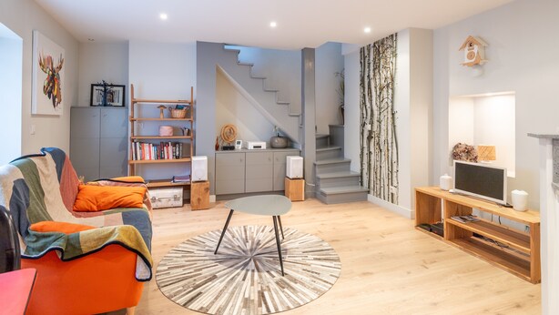 A modern living room with a sofa, a coffee table, and a TV stand. There is a staircase leading to another level.