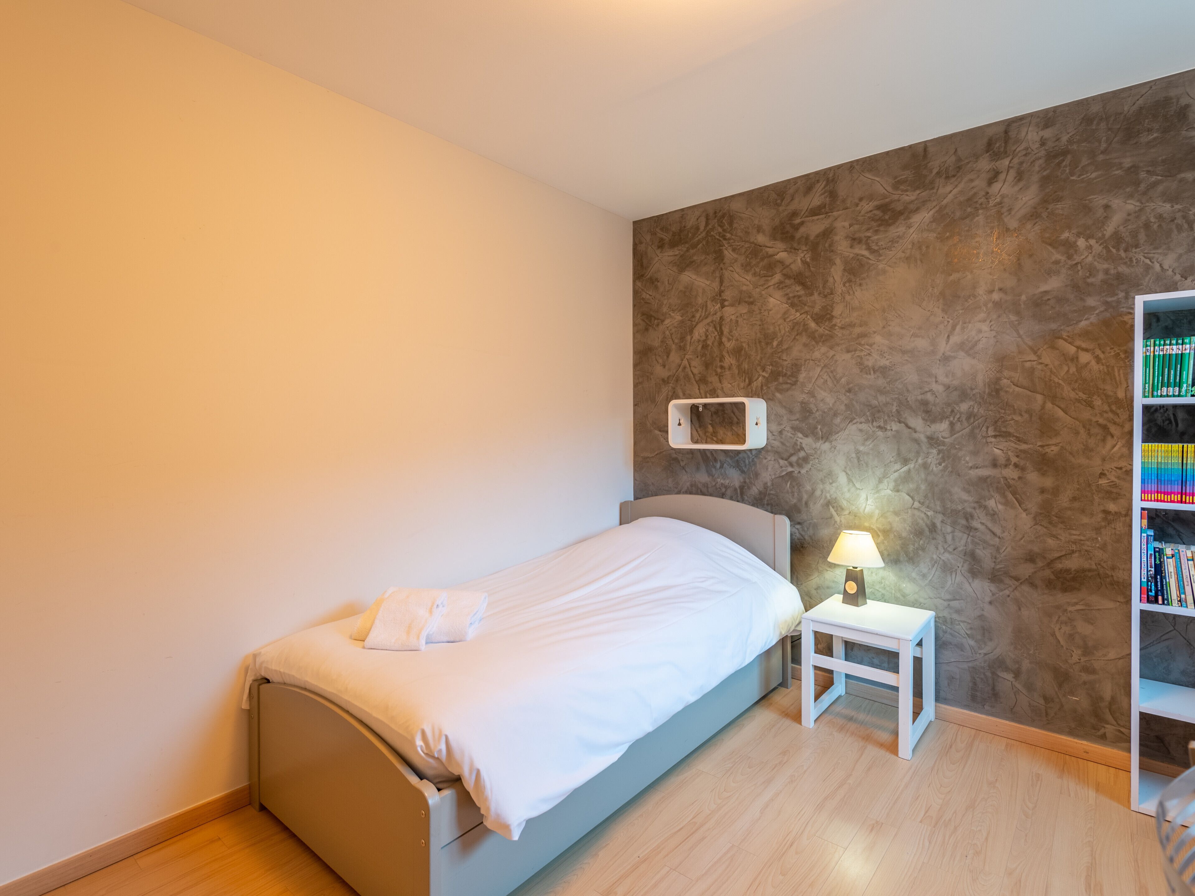 A bedroom with a bed, bedside table, lamp, and a bookshelf.