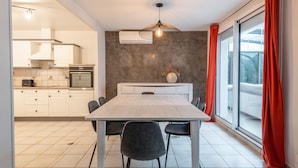 Een moderne keuken met witte kasten, een inbouwoven en een eethoek met een grote tafel en stoelen.