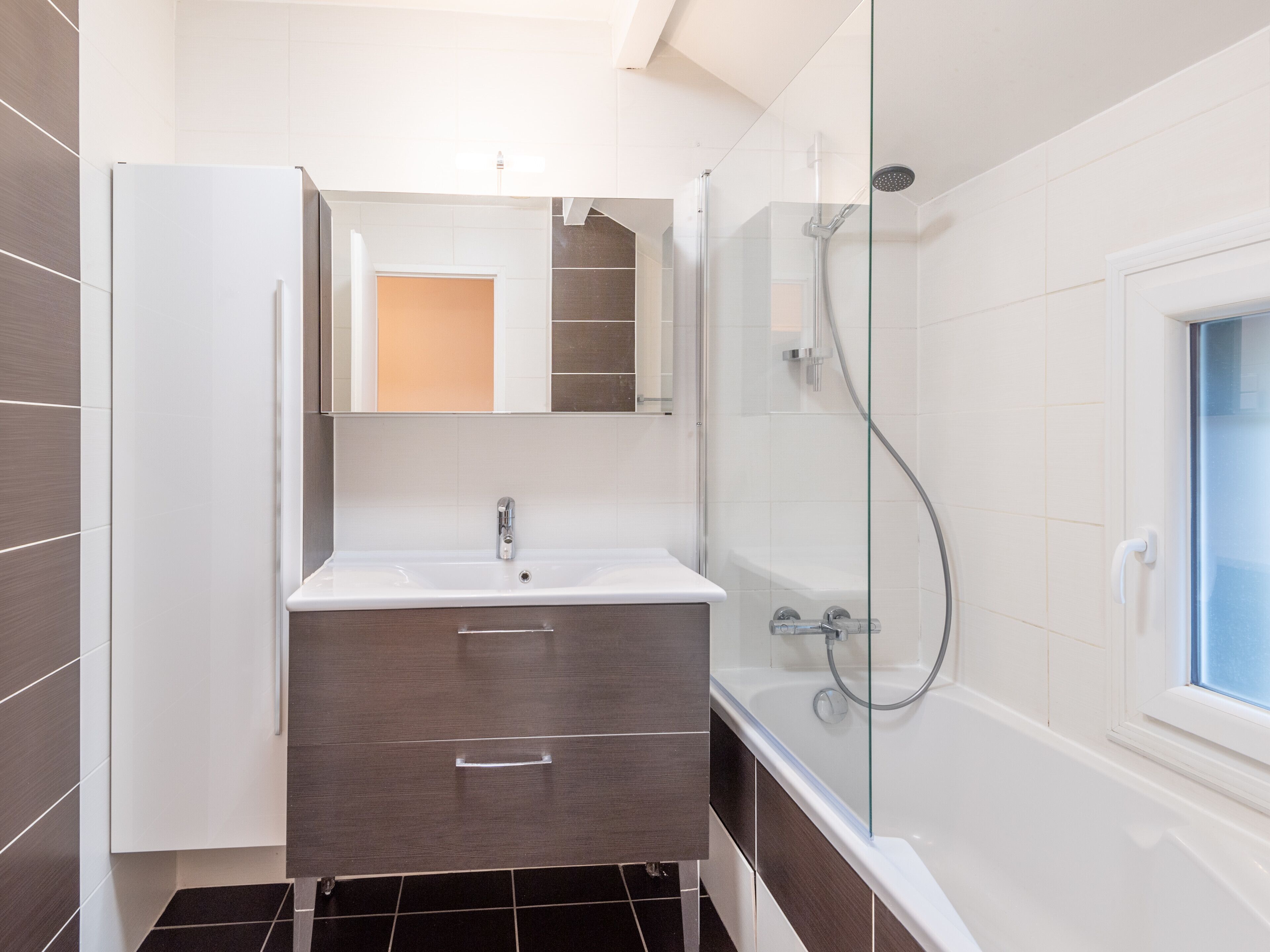 Une salle de bain moderne avec une douche à parois de verre, un lavabo blanc et des meubles de rangement aux tons foncés.