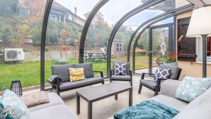 Een overdekt terras met een bank, stoelen en een tafel.