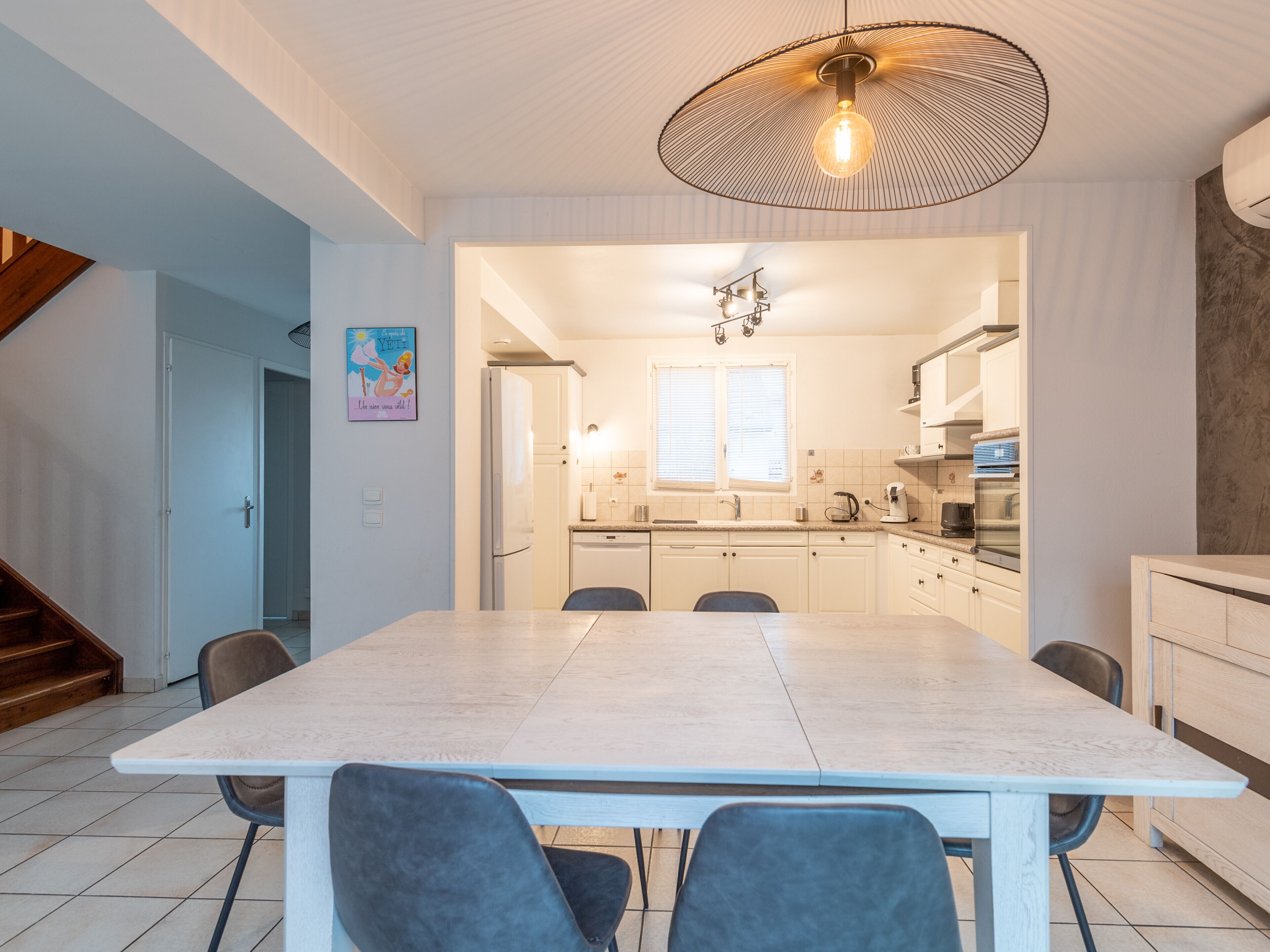 A modern kitchen with white cabinets, a dining table with chairs, and a unique ceiling light fixture.