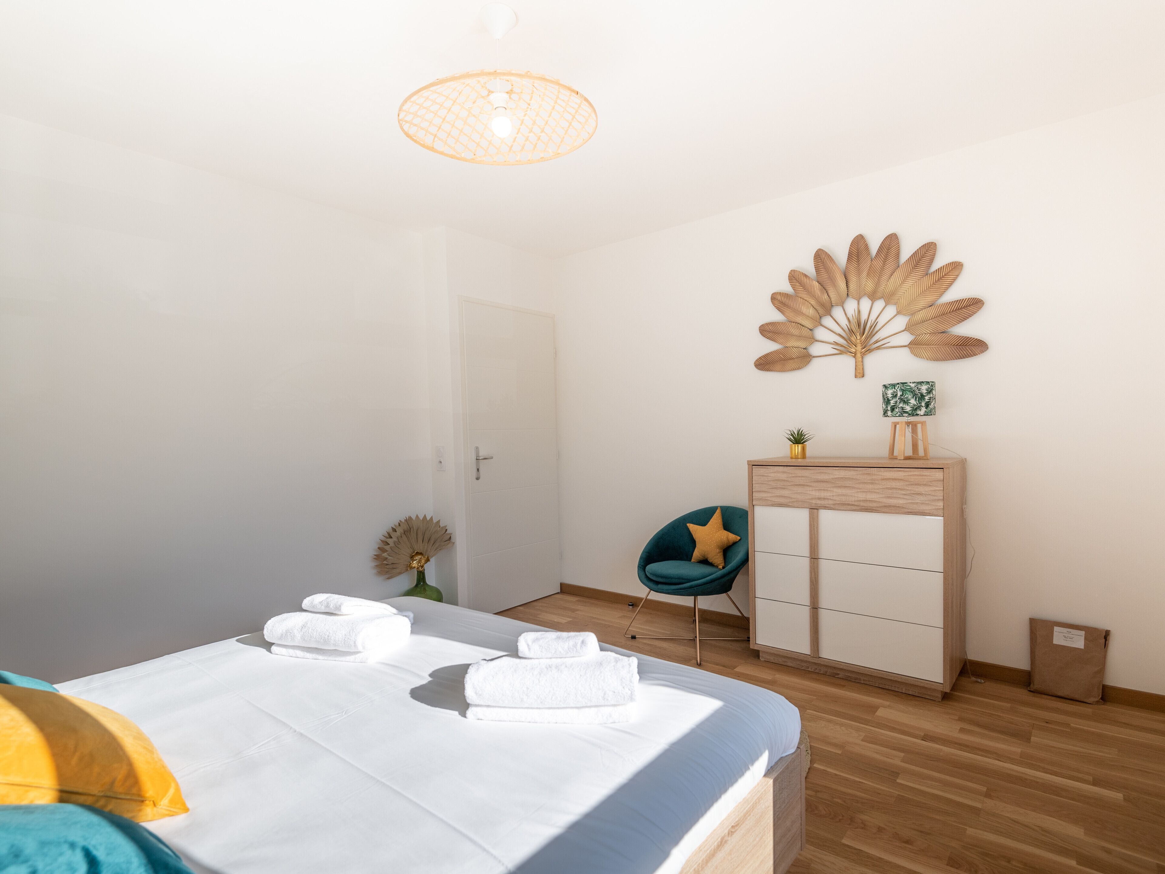 A bedroom with a bed, a desk, a chair, a decorative wall piece, and a small plant.