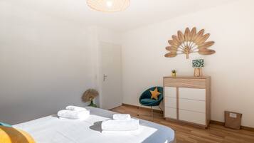 A bedroom with a bed, a desk, a chair, a decorative wall piece, and a small plant.