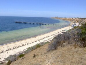 A beach with a long pier extending into the sea, a sandy shore, and a hilly landscape in the background. - Yaringa - Close to beach, Off Peak Special! (Wool Bay)