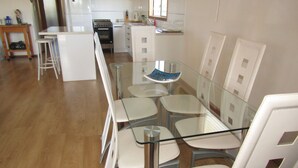 Eine moderne Küche mit weißen Geräten, einem Glastisch und weißen Stühlen.