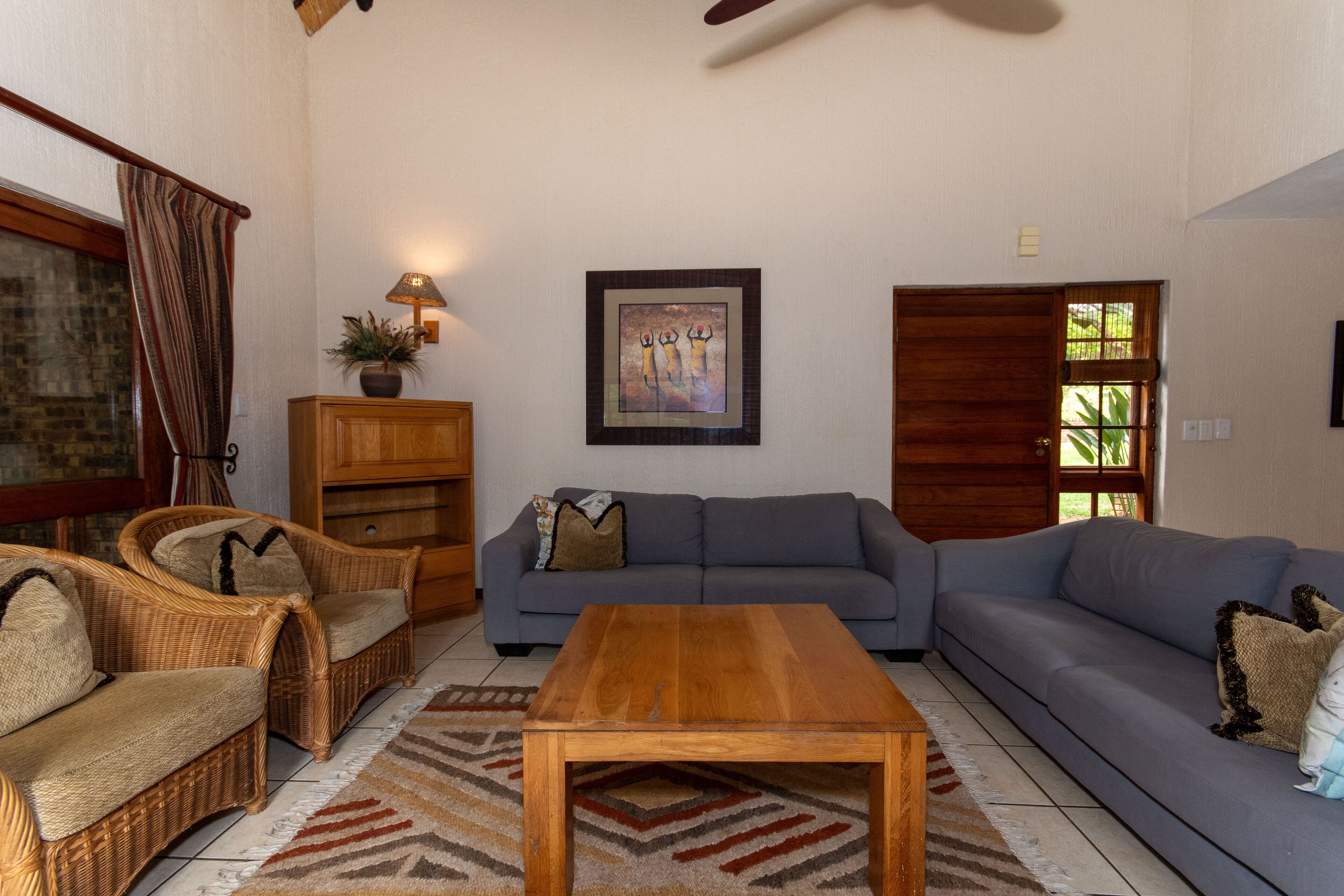 A living room with a sofa, two wicker chairs, a wooden coffee table, a lamp, and a framed artwork on the wall.