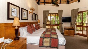 Habitación de hotel con una cama grande, cabecera de madera, televisor de pantalla plana, teléfono, lámpara y cuadros en la pared.
