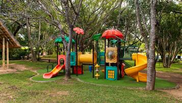 Un parque infantil con toboganes y estructuras para escalar, rodeado de árboles.
