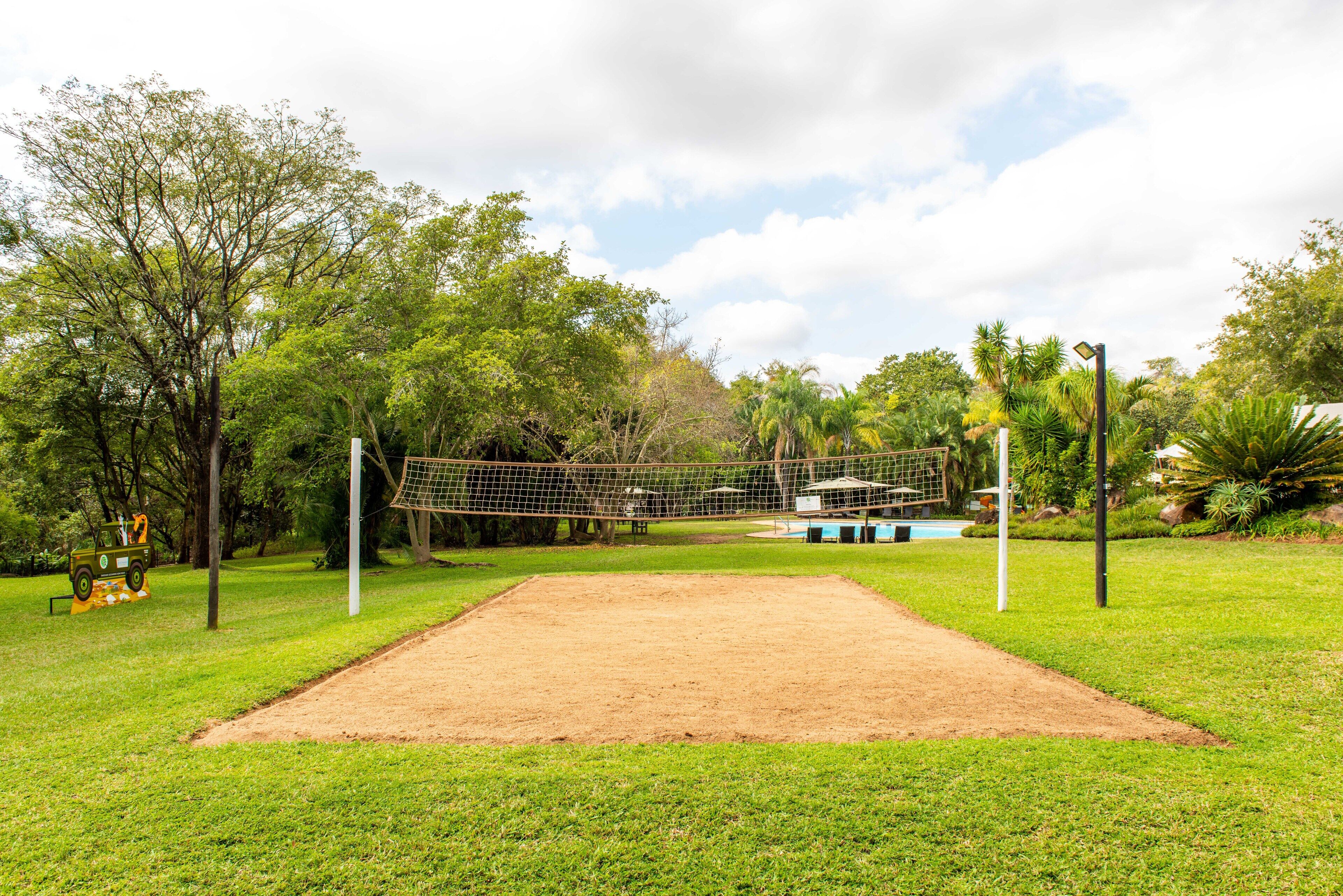 A volleyball court surrounded by trees and a small vehicle.