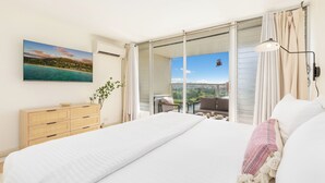 Un dormitorio con una cama grande, un aparador de madera, una planta y un balcón con vista al mar.