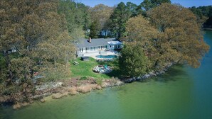Vue aérienne d’une maison avec une piscine, entourée d’arbres et bordée d’un lac.