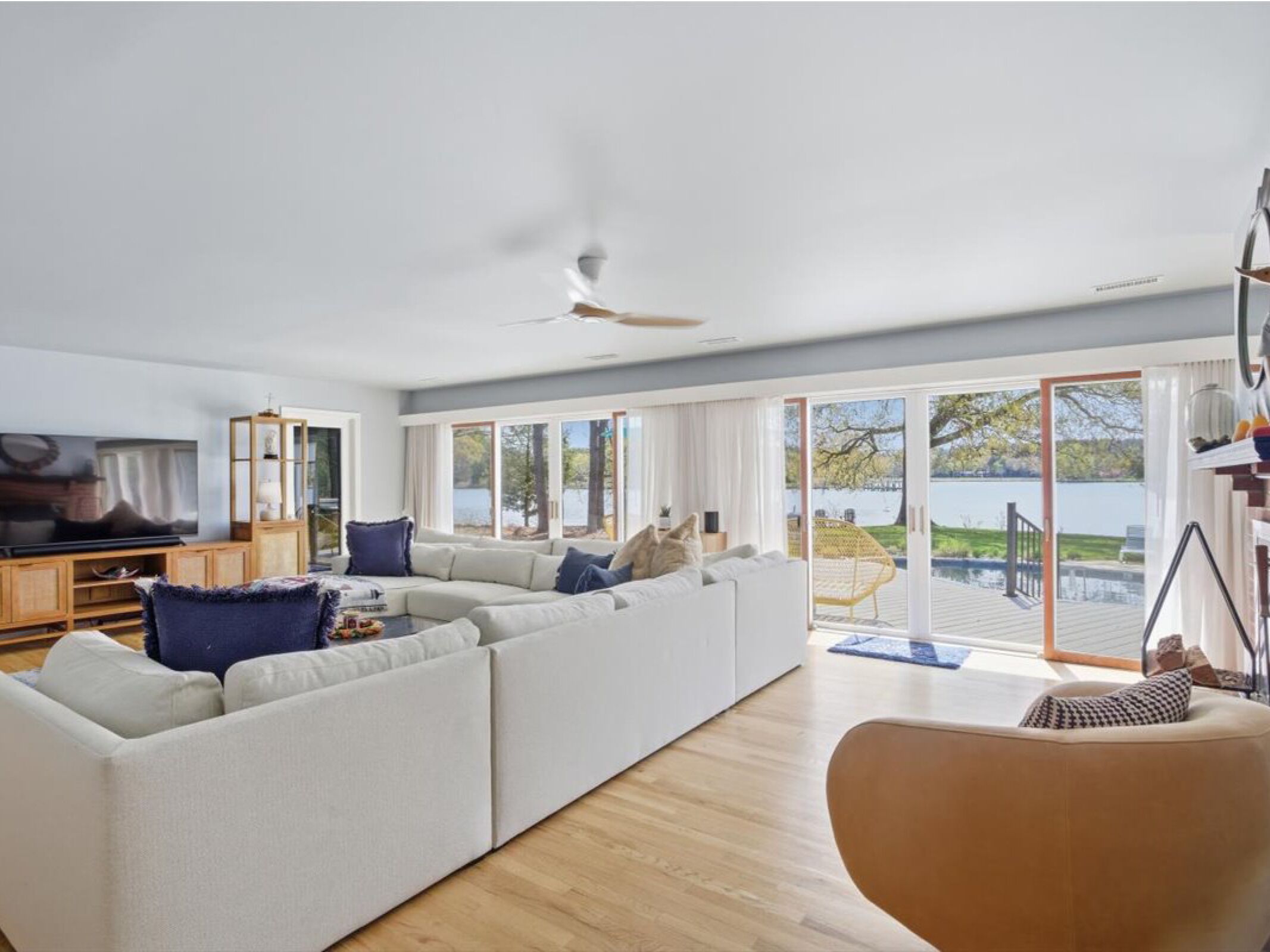 Un salon moderne avec un canapé d’angle, un téléviseur et une vue sur un lac, grâce à de grandes fenêtres.