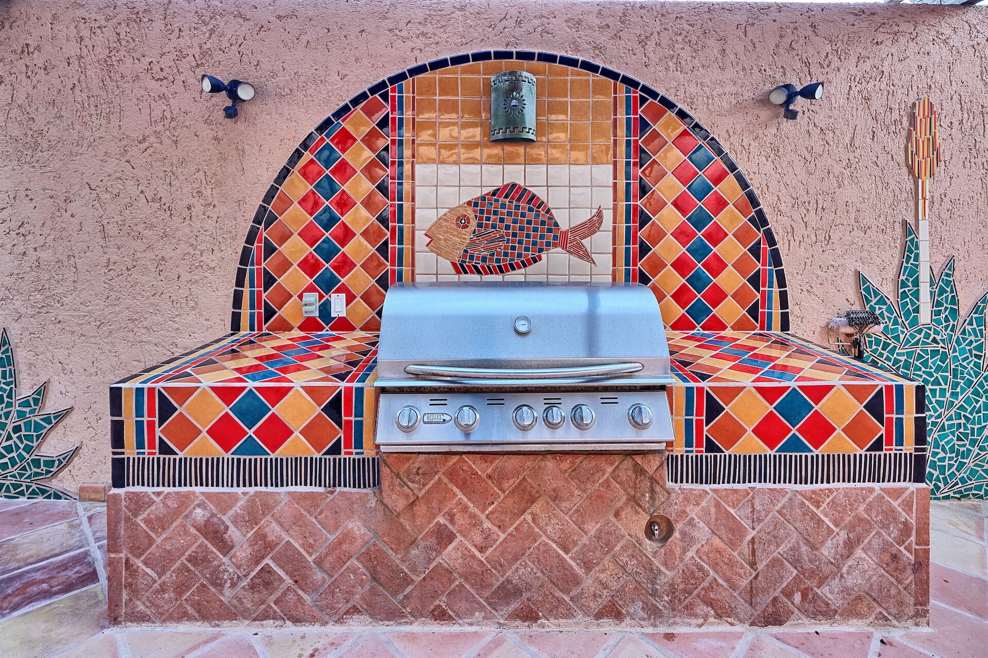 Una parrilla para barbacoa al aire libre con un respaldas de mosaico de colores y un diseño de pez.