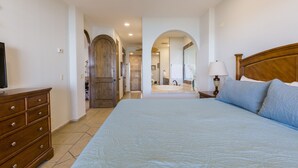 Een slaapkamer met een groot bed, een houten dressoir, een televisie, en een badkamer die door een boog zichtbaar is.