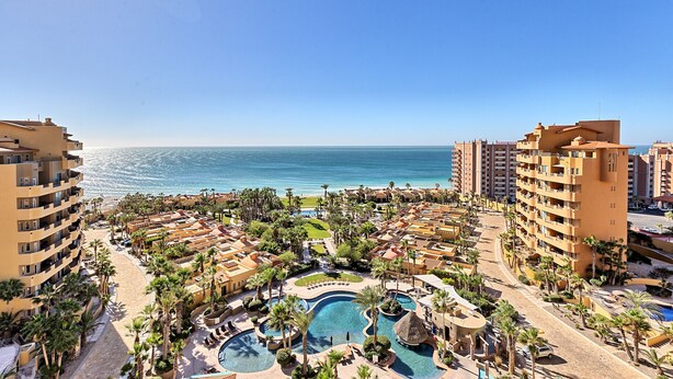 Een resort met meerdere zwembaden, palmbomen en uitzicht op de oceaan.
