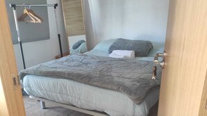 A bedroom with a bed, a hanging wardrobe, a mirror, and a door. - Chez Moustapha (San Juan de Aznalfarache)