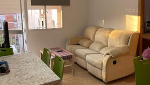 A living room with a beige sofa, a dining table with chairs, and a hanging light fixture. - Chez Moustapha (San Juan de Aznalfarache)