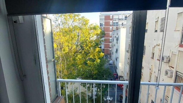 A view from a balcony with a metal railing, overlooking a street with buildings and a tree with yellow leaves. - Chez Moustapha (San Juan de Aznalfarache)