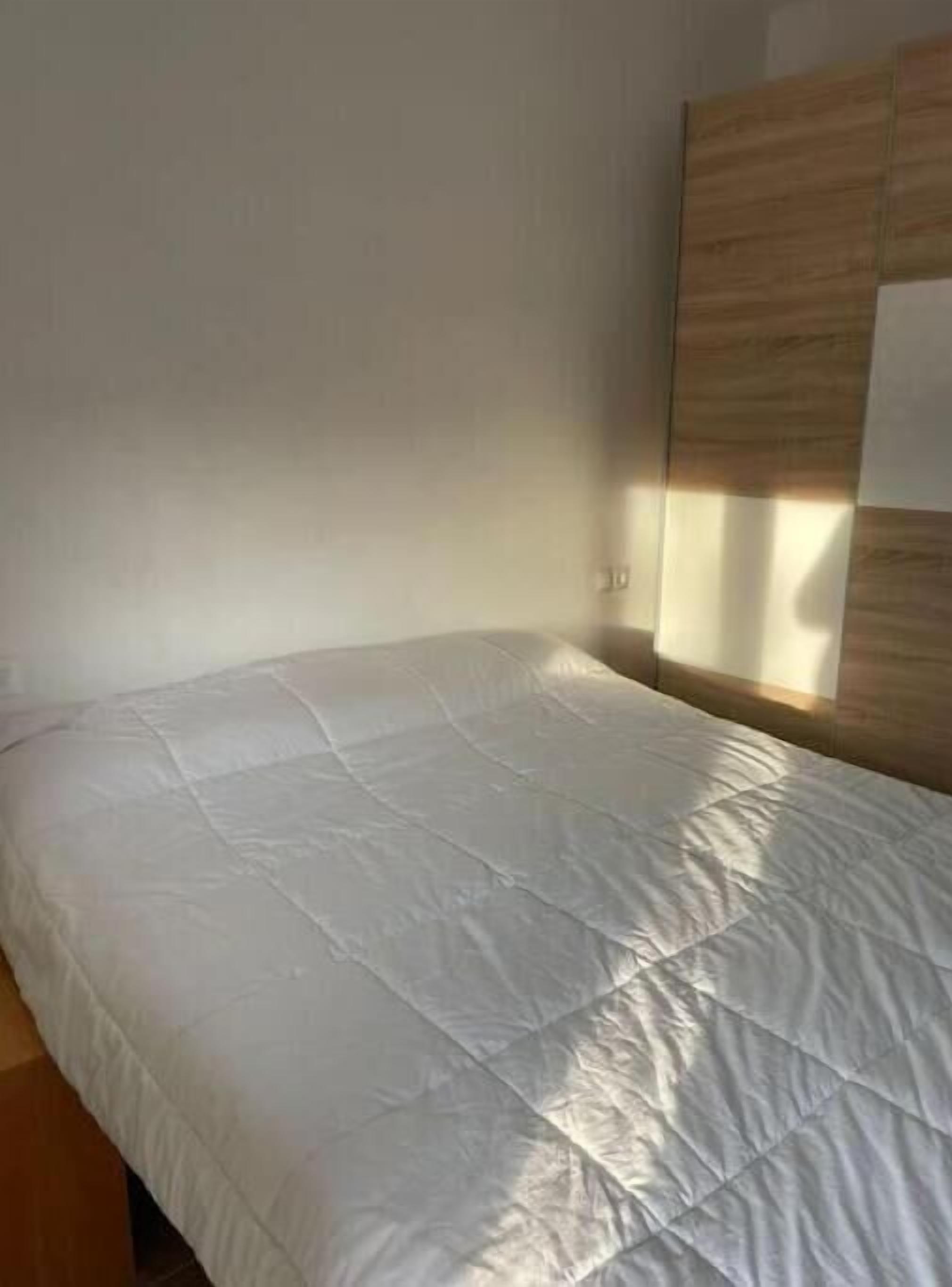 Una cama individual con colchón blanco en una habitación con cabecera de madera y pared lisa.