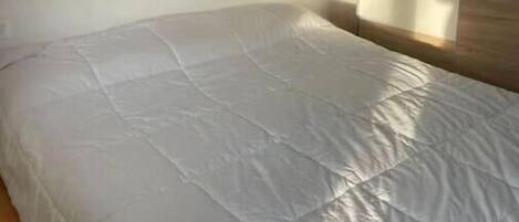 Una cama individual con colchón blanco en una habitación con cabecera de madera y pared lisa.