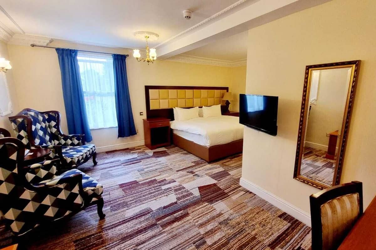 Ein Hotelzimmer mit einem Bett, einem Fernseher, einem Spiegel und gepolsterten Sesseln mit Muster.