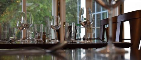 A dining table with several wine glasses and a pitcher, set against a window with a view of greenery.