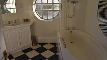 A bathroom with a checkered floor, a bathtub, a shower, and a round window.